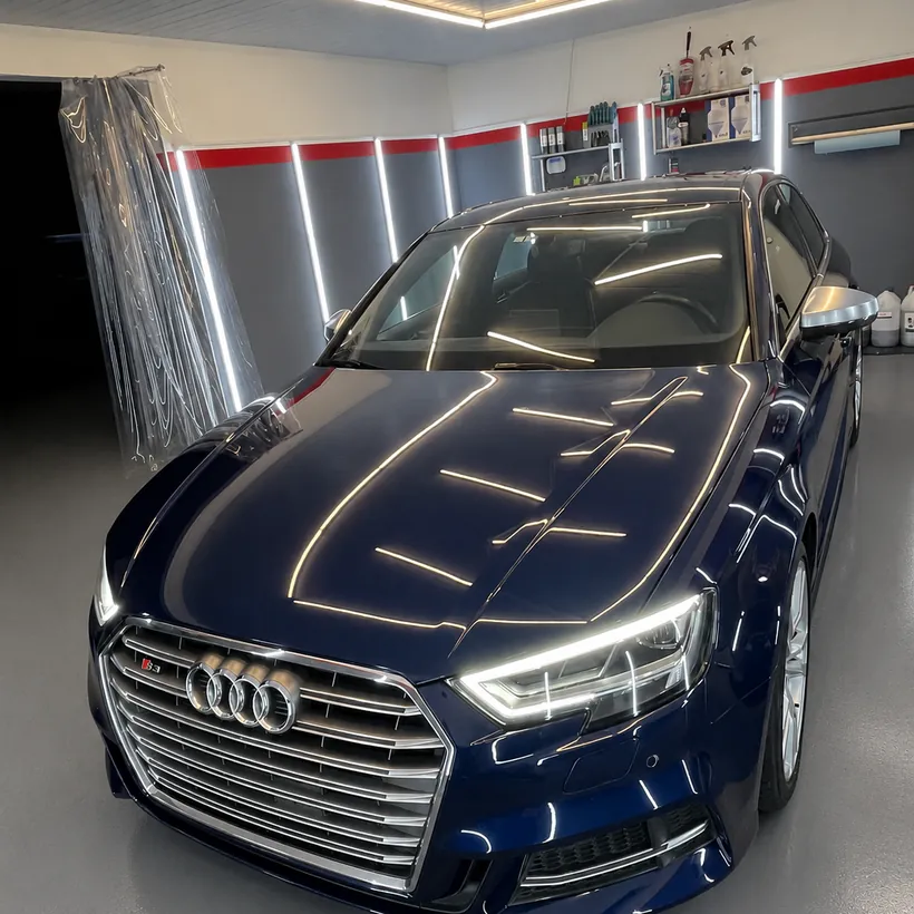 Audi azul oscuro de frente, con el reflejo de las luces sobre el capo
